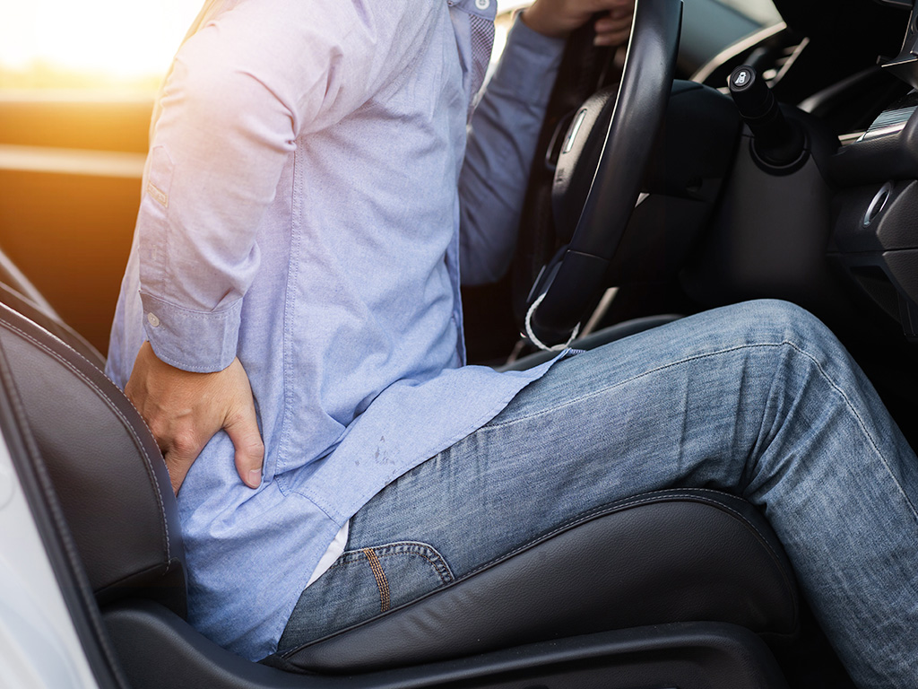 Person experiencing lower back pain while sitting in a vehicle after a collision.