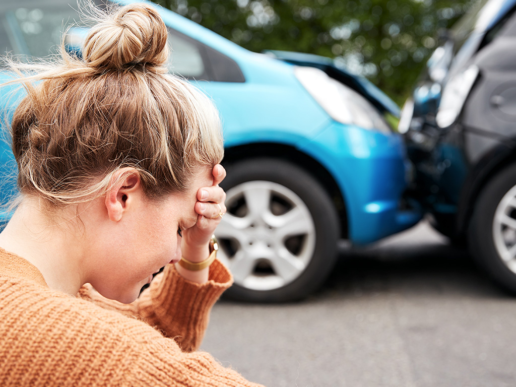 Person appearing distressed after a motor vehicle accident involving two damaged vehicles.