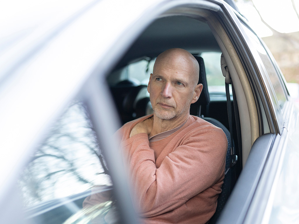 Accident victim experiencing shoulder pain while sitting inside a vehicle.